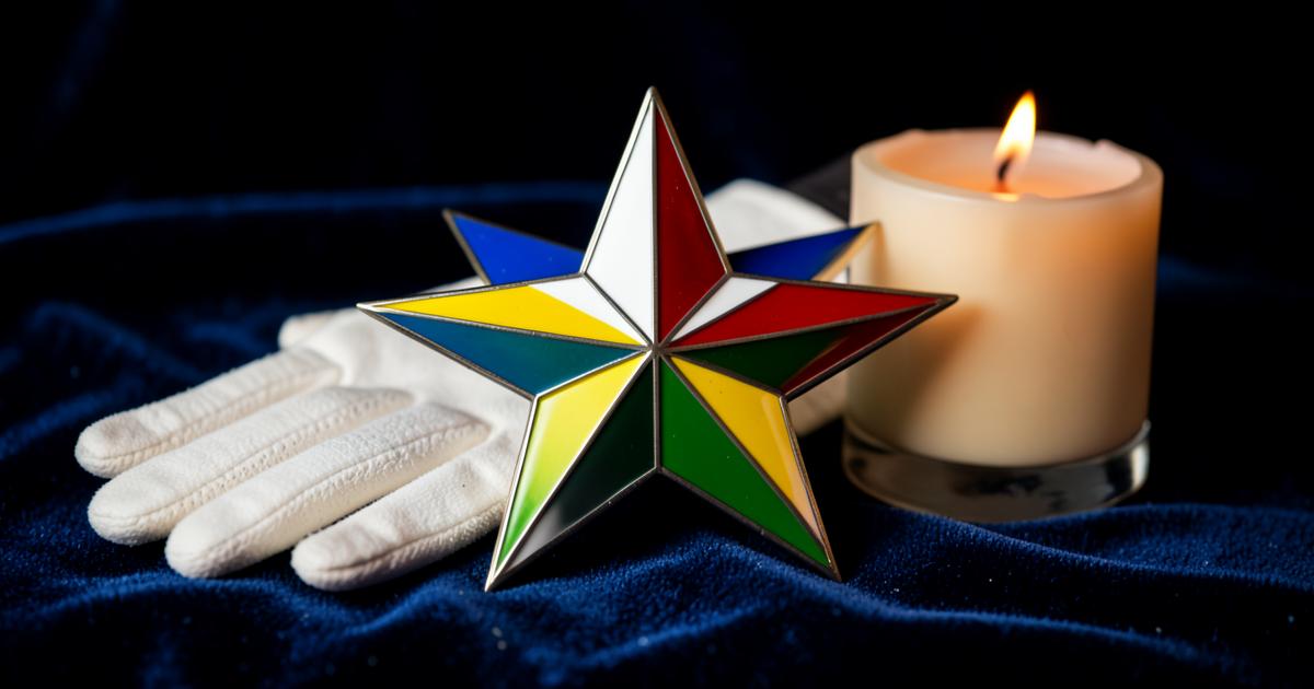Emblema da estrela de cinco pontas em cores sobre veludo azul, ao lado de luva branca e vela acesa