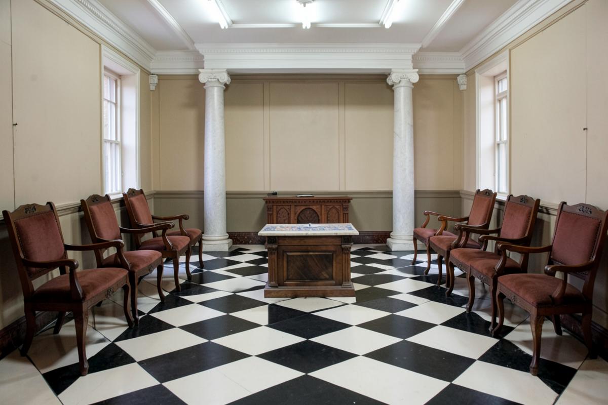 Sala de uma Loja maçônica com piso em xadrez preto e branco, colunas, poltronas laterais e um altar central de madeira