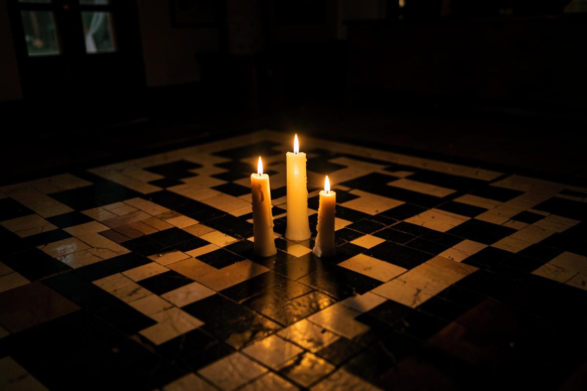 Três velas acesas dispostas em triângulo sobre o piso mosaico de uma Loja